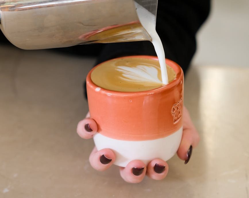 Una persona sirve leche en una taza de café